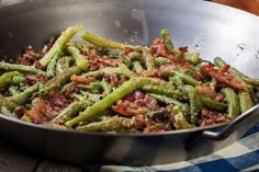 green beans and bacon cooking in a pan on a wooden table with a blue towel