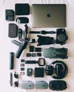 an assortment of electronics and accessories laid out on a white blanket with a laptop in the background