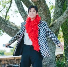 a man with a red scarf around his neck standing in front of a large tree