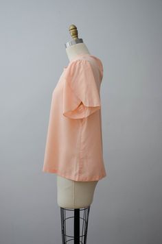 A short sleeve peach T-shirt with an embroidered neckline and tulip flutter sleeves. ☛ m e a s u r e m e n t s ☚ Bust: 42 Waist: 44 Shoulders: 16 Length: 24 ☛ d e t a i l s ☚ Era: 1980s Material: polyester/cotton Condition: excellent ☛ m o r e t o p s ☚ https://etsy.me/2PKyN5U ☛ v i s i t t h e s h o p ☚ https://etsy.me/2Nd23kg ☛ instagram ┇ poppycockvintage ☛ facebook ┇ poppycockvintage Spring Heather Peach Short Sleeve T-shirt, Heather Peach Short Sleeve T-shirt For Spring, Heather Peach Short Sleeve Tops For Summer, Peach Short Sleeve Blouse For Summer, Peach Short Sleeve Summer Blouse, Peach Short Sleeve Summer Tops, Feminine Short Sleeve T-shirt For Summer, Feminine Short Sleeve Summer T-shirt, Heather Peach Short Sleeve Relaxed Fit Top