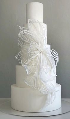 a three tiered white wedding cake with feathers on it