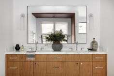 a bathroom vanity with two sinks and a large mirror above it, in front of a window