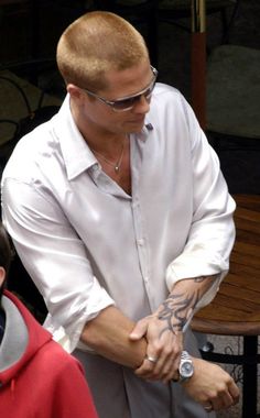 a man in white shirt and sunglasses standing next to another man with tattoos on his arm