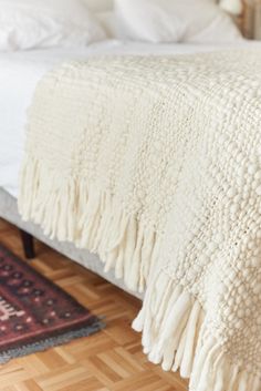 a bed with a white blanket on top of it next to a rug and pillows