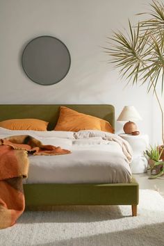 a bed with orange and white sheets in a bedroom next to a plant on the wall