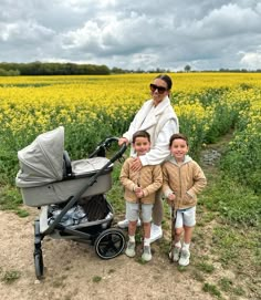 a woman standing next to two children in front of a field full of yellow flowers