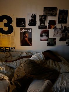 a man laying on top of a bed in a bedroom next to a wall with posters