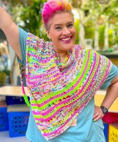 a woman with pink hair wearing a multicolored shawl and smiling at the camera