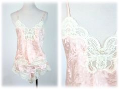 Vintage 1980s camisole and tap pants set. Pale pink, silky polyester has a shadow print. Trimmed with cream lace. Top has spaghetti straps. Tap pants have elastic waist meant to be worn at the waist with high cut legs. Label reads, "Lucie Ann II, made in the USA." Pants are marked size small and I believe the cami is size 34 (the label is a bit worn). Freshly laundered. Excellent condition.  Measurements: Camisole Bust = 34" Waist = 34" Length from top of shoulder to hem = 20" Pants Waist = 18" - 28" Hips = 40" Length from waist to middle of crotch = 13.5" All measurements are taken with the garment flat, doubled for the bust (chest), waist, hips, and circumference. Please make sure you leave yourself a little wiggle room for a comfortable fit! Some garments may be clipped to show proper f Pink Lace Trim Camisole In Coquette Style, Pink Lace Trim Coquette Camisole, Pink Lace Camisole In Coquette Style, Pink Lace Coquette Camisole, Pink Satin Camisole, Vintage Pink Fitted Camisole, Pink Fitted Vintage Camisole, Pink Lace Trim Camisole For Pajama Party, Pink Fitted Camisole For Pajama Party