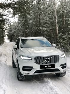 a white car driving down a snow covered road in front of some trees and bushes