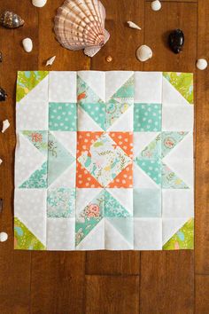 a quilted table runner with shells and seashells around it on a wooden surface