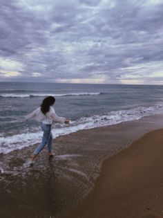 a woman is running on the beach in front of the ocean with her arms outstretched