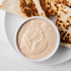 some pita bread and dip are on a white plate with a small bowl of dipping sauce