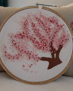 a close up of a embroidery on a pillow with a tree in the middle and red flowers