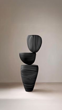 three black vases stacked on top of each other in front of a beige wall