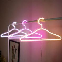 three neon clothes hangers in front of a pink wall with a framed picture on it