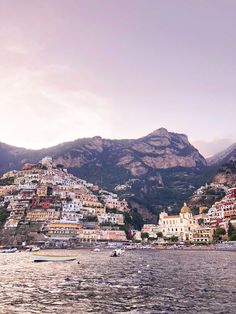 boats are on the water in front of some buildings and mountains with houses on them