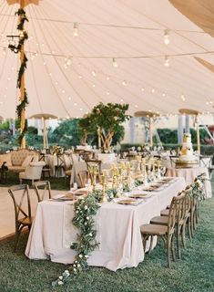 an outdoor tent with tables and chairs covered in white linens, greenery and candles