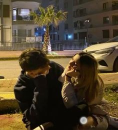 a man sitting on the ground talking on a cell phone next to a young woman