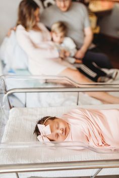 a woman laying in a hospital bed next to two children and an adult holding a baby