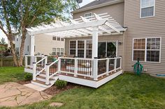 a deck with white railing and trellis on it in front of a house next to a tree