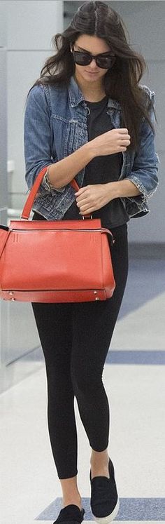 a woman walking through an airport carrying a red handbag and her luggage behind her