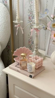 a white dresser topped with candles and pink flowers next to a mirror on top of it