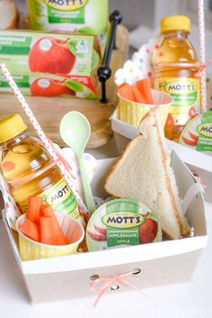 a lunch box filled with fruit, juice and sandwiches on top of a white table