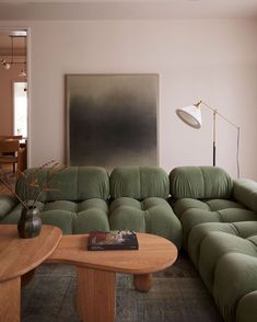 a living room filled with green couches and a wooden coffee table in front of a painting on the wall