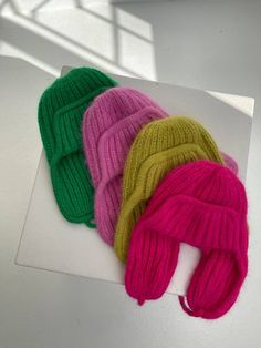 three knitted hats sitting on top of a white table next to each other in different colors