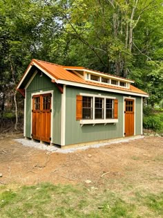 a small green shed with wooden doors and windows on the roof is in front of some trees