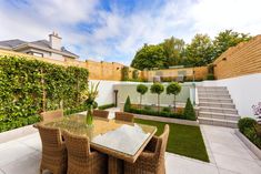 an outdoor dining area with wicker chairs and table surrounded by greenery in the back yard