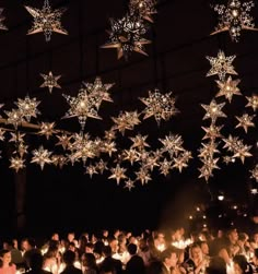 a large group of people standing around each other holding lit candles in front of stars hanging from the ceiling