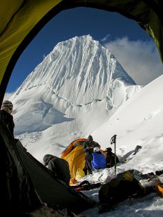 two people are camping in the snow next to a mountain