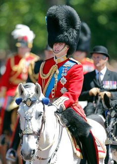 a man riding on the back of a white horse next to other men in uniform