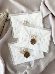 two white envelopes with gold buttons and pearls on them are laying next to a rock