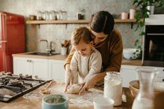 a woman and child are making dough in the kitchen