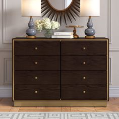 a dresser with two lamps and a mirror above it on the wall next to a rug