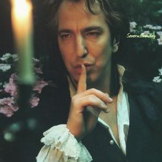 a man with his finger in his mouth next to a lit candle and some flowers