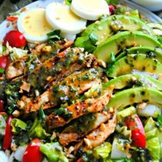 a salad with chicken, avocado, tomatoes and other veggies on it