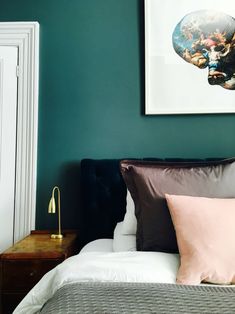 a bed in a bedroom with green walls and paintings on the wall above it's headboard