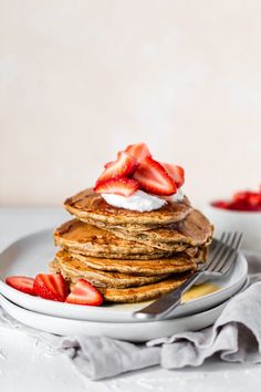 a stack of pancakes topped with whipped cream and strawberries on a plate next to a fork