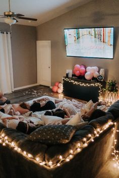 two people laying on a couch watching tv in a living room with lights all around