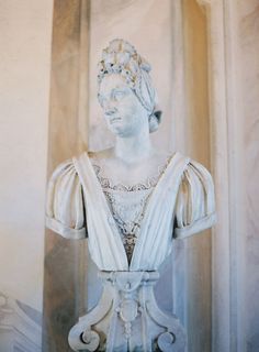 a statue of a woman wearing a tiara in front of a wall with columns