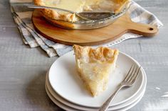 a piece of pie on a plate with a fork next to it and a glass dish