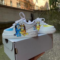 someone is holding up a pair of sneakers with cartoon characters painted on the upper part of them