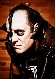 a man with black makeup and horns on his head wearing a leather jacket in front of a brick wall