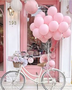 a bicycle parked in front of a store with pink balloons attached to the handlebars