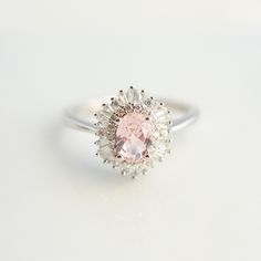 an oval shaped pink diamond ring on a white surface with small diamonds around the band