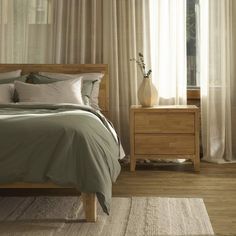 a bed sitting next to a window covered in white drapes and pillows on top of a wooden floor